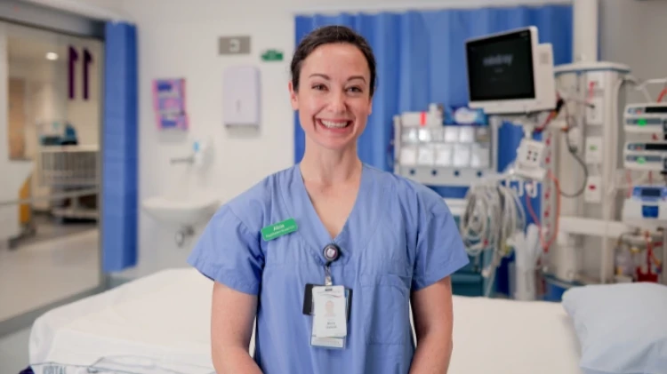 Critical Care Nurse Alicia standing in front of a vacant hospital bed in the patients' ward.