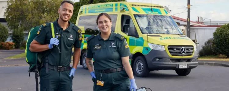 Two ambulance officers standing in front of a St. Johns ambulance with their gear in a parking lot.