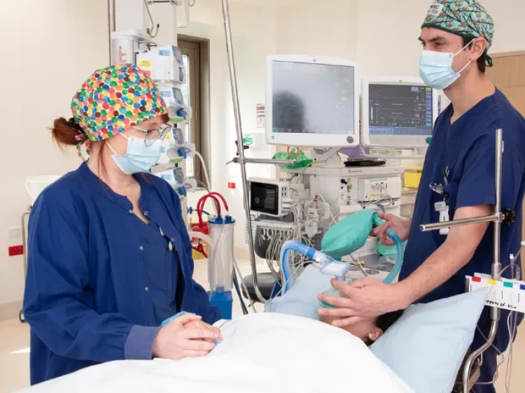 Two Anaesthetic Technicians preparing anaesthesia for a patient lying on a hospital bed prior to surgery.