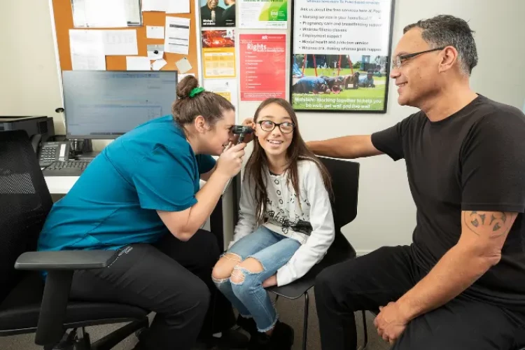 A community nurse looking through an otoscope to check the ear of a young patient