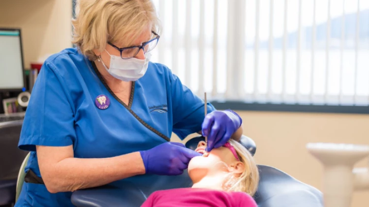 A community dental nurse examining a young patient's teeth on the dentist's chair.