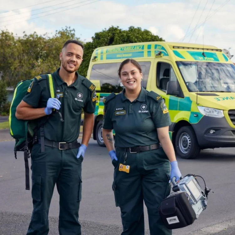 Two ambulance officers standing in front of a St. Johns ambulance with their gear in a parking lot.