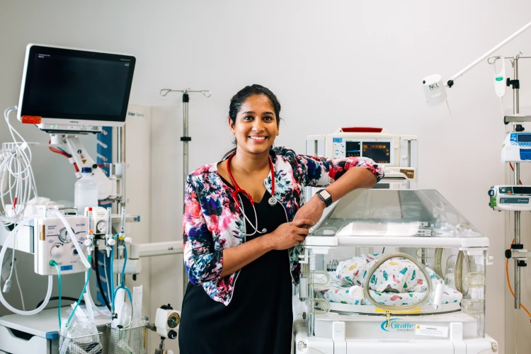 An RMO stands with her left arm resting on a vacant incubator