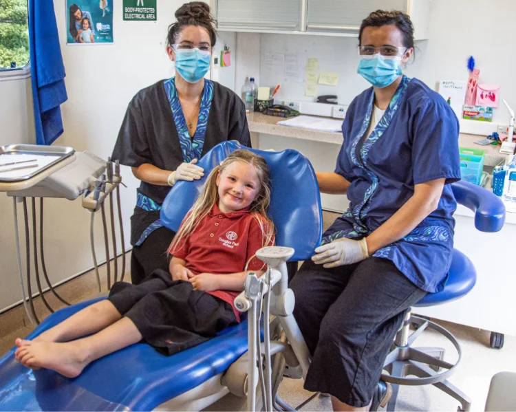 Two Oral Health Therapists sitting on either side of a primary school aged patient for her dental treatment.