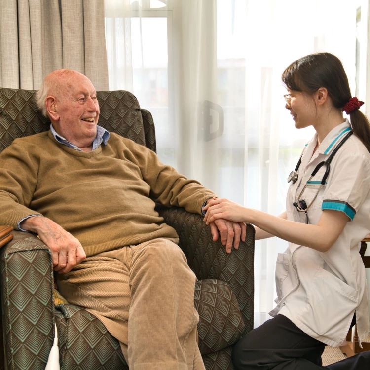 Aged care Nurse Pearl supportively checking up on an elderly patient sitting comfortably