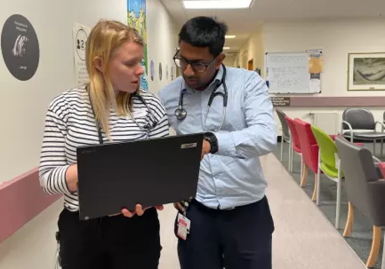 Two Radiation Oncologists walking together discussing over a result on a laptop.